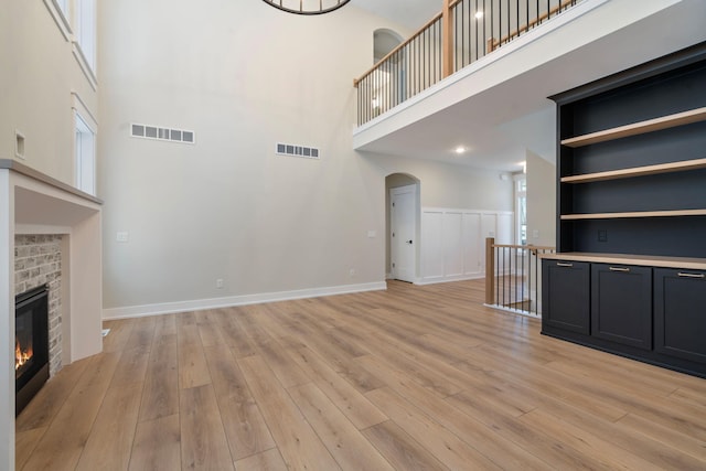 unfurnished living room featuring a towering ceiling, built in shelves, light wood-type flooring, and a brick fireplace