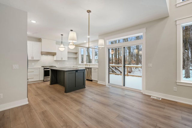 kitchen featuring appliances with stainless steel finishes, a center island, pendant lighting, white cabinets, and wall chimney range hood