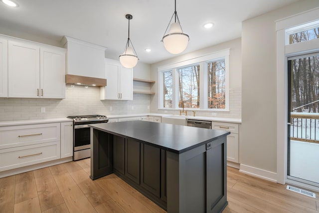 kitchen featuring white cabinetry, a center island, light wood-type flooring, hanging light fixtures, and appliances with stainless steel finishes