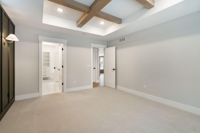 unfurnished bedroom with light carpet, a closet, beam ceiling, a walk in closet, and coffered ceiling