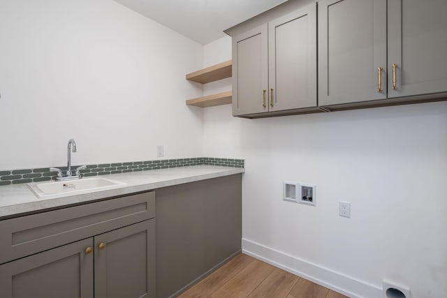 clothes washing area featuring sink, light hardwood / wood-style floors, hookup for a washing machine, and cabinets