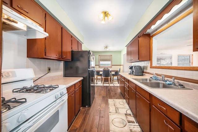 kitchen with white range with gas cooktop, black fridge, dark hardwood / wood-style flooring, sink, and backsplash