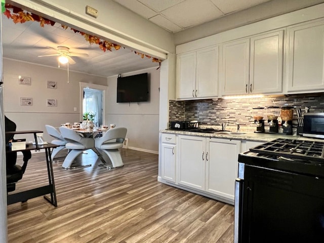 kitchen featuring white cabinetry, a drop ceiling, gas range oven, ceiling fan, and decorative backsplash