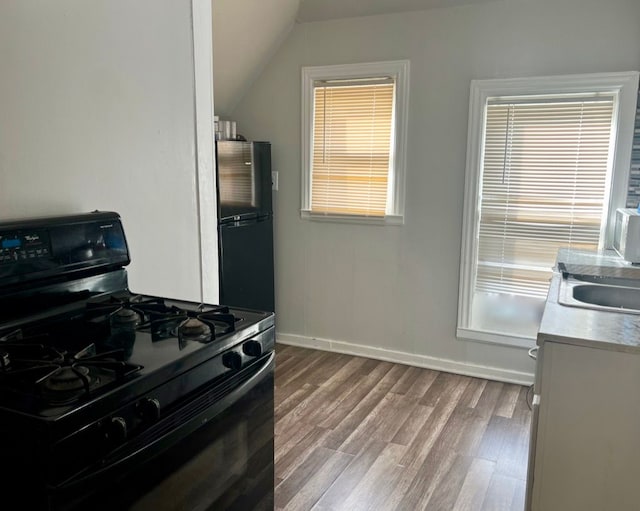 kitchen with black range with gas cooktop, vaulted ceiling, wood-type flooring, stainless steel fridge, and sink