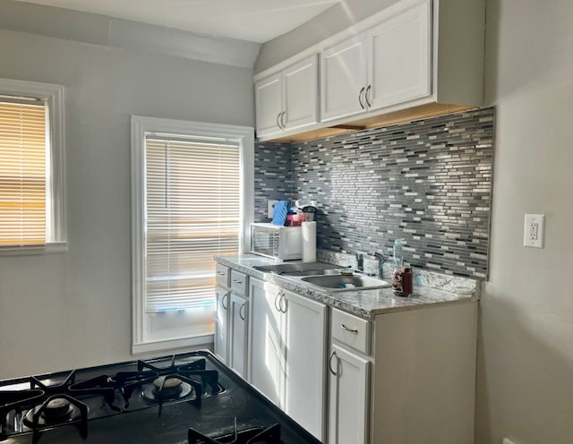 kitchen with white cabinets, cooktop, sink, and tasteful backsplash