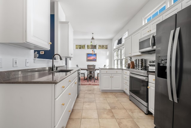 kitchen with appliances with stainless steel finishes, light tile patterned floors, white cabinets, decorative light fixtures, and sink