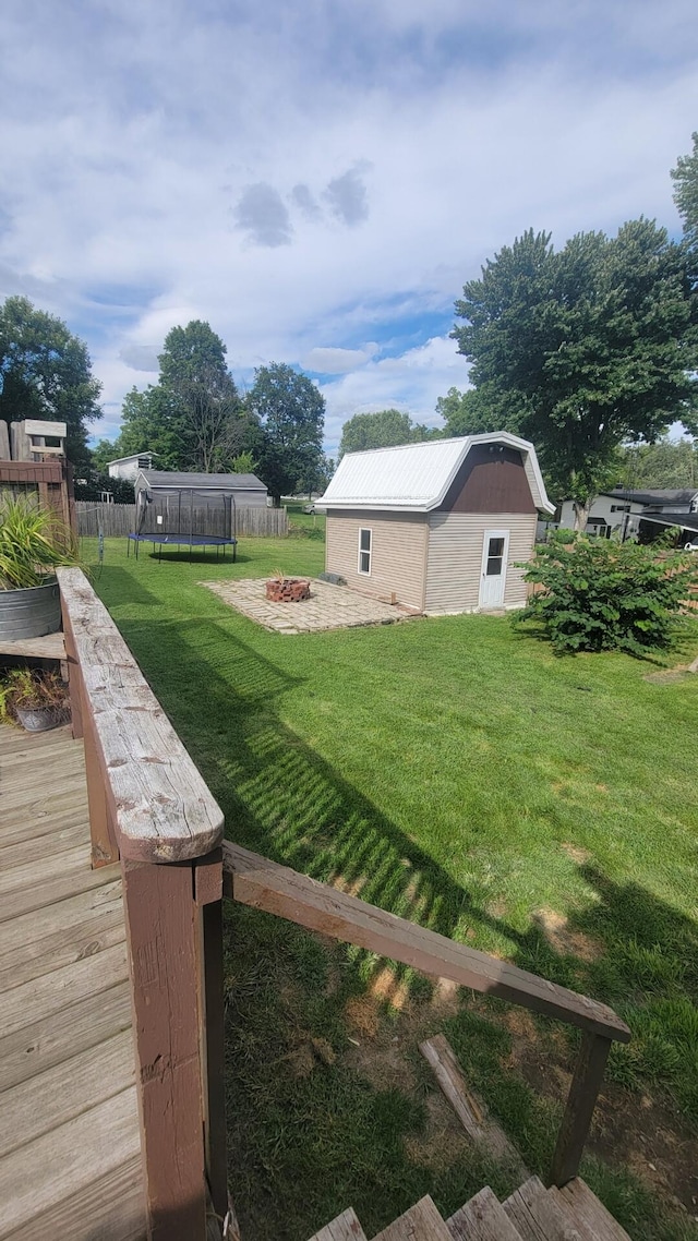 view of yard featuring a fire pit, a deck, a storage shed, and a trampoline