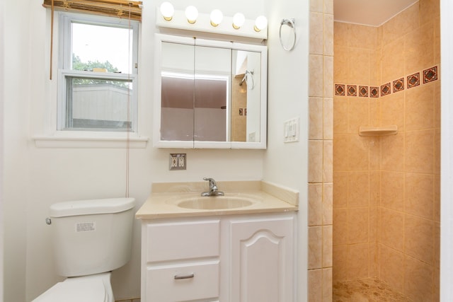 bathroom featuring toilet, tiled shower, and vanity