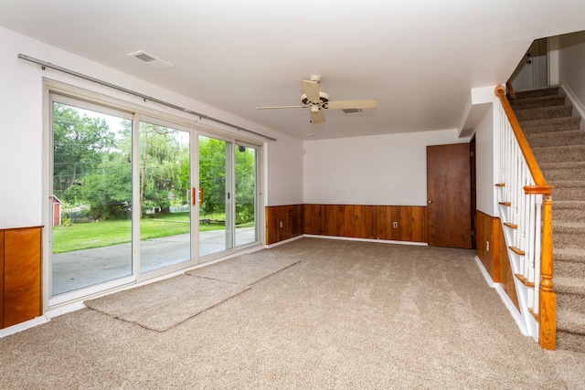 carpeted spare room featuring wood walls and ceiling fan