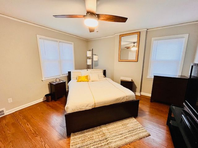 bedroom with ceiling fan, multiple windows, hardwood / wood-style floors, and ornamental molding