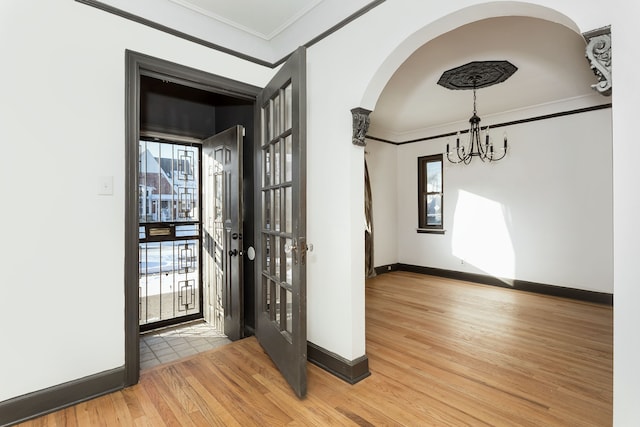 entryway featuring hardwood / wood-style flooring, ornamental molding, french doors, and an inviting chandelier