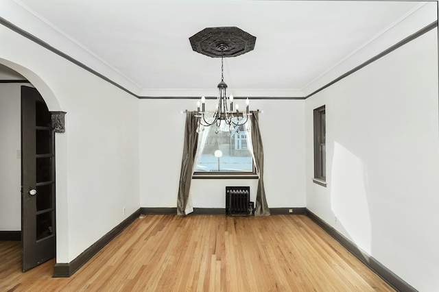 unfurnished dining area featuring wood-type flooring, radiator, ornamental molding, and an inviting chandelier