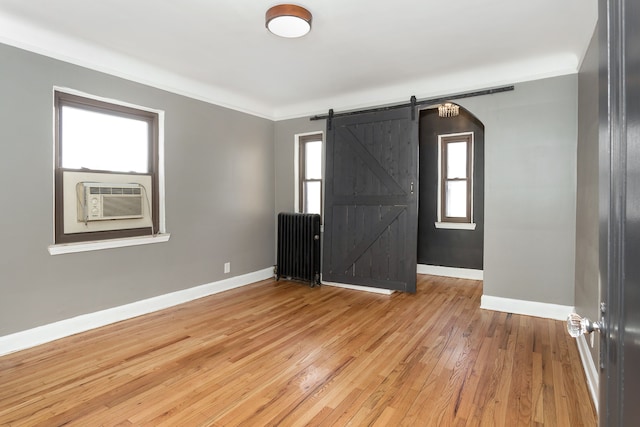 unfurnished room with plenty of natural light, radiator, a barn door, and light hardwood / wood-style flooring