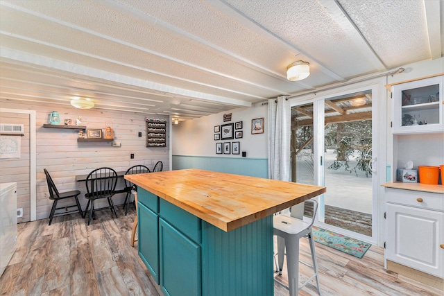 kitchen with wooden walls, a kitchen bar, wooden counters, hardwood / wood-style floors, and white cabinets