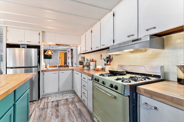 kitchen featuring white gas stove, white cabinetry, butcher block countertops, stainless steel refrigerator, and pendant lighting