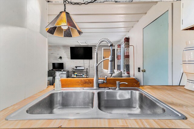 kitchen with sink, white cabinets, decorative light fixtures, and wood walls