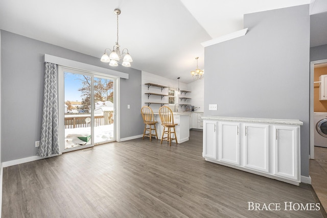 unfurnished dining area with washer / clothes dryer, dark hardwood / wood-style flooring, an inviting chandelier, and vaulted ceiling