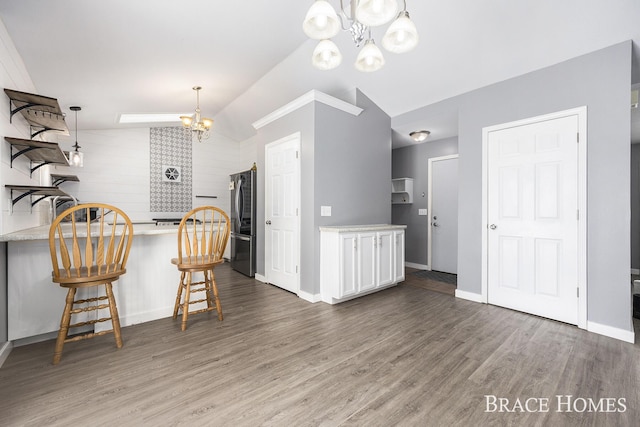 kitchen featuring white cabinets, lofted ceiling, a kitchen bar, stainless steel fridge, and a chandelier