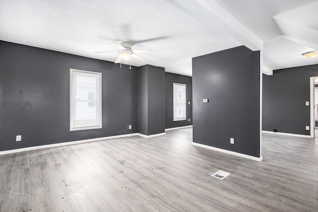 empty room featuring ceiling fan, dark hardwood / wood-style flooring, and beamed ceiling