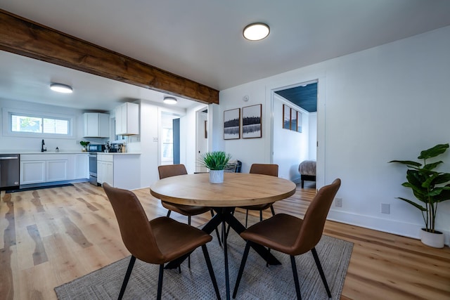 dining area featuring light hardwood / wood-style flooring, beamed ceiling, and sink