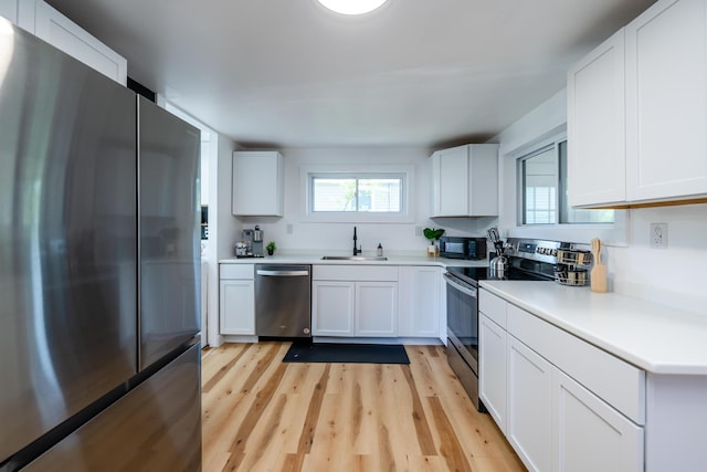 kitchen with sink, white cabinets, light hardwood / wood-style floors, and appliances with stainless steel finishes