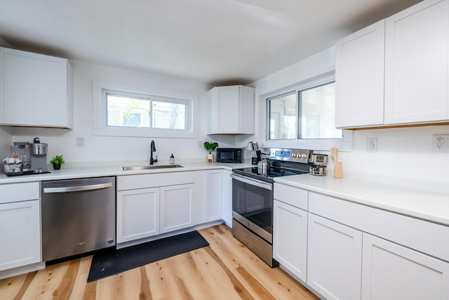 kitchen with stainless steel appliances, light wood-type flooring, white cabinetry, and sink