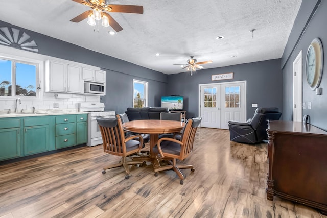 dining room with sink, a textured ceiling, french doors, light wood-type flooring, and ceiling fan