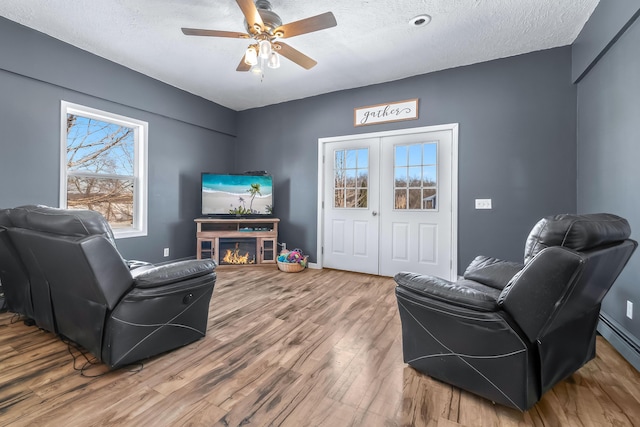 sitting room with a textured ceiling, french doors, hardwood / wood-style floors, baseboard heating, and ceiling fan