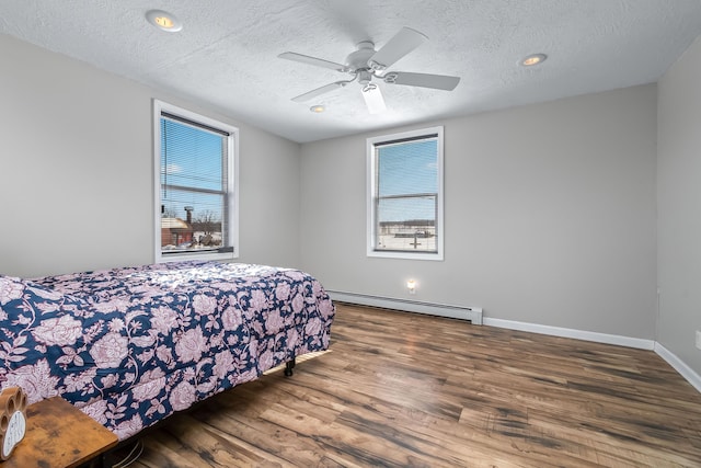 bedroom with baseboard heating, a textured ceiling, dark wood-type flooring, and ceiling fan