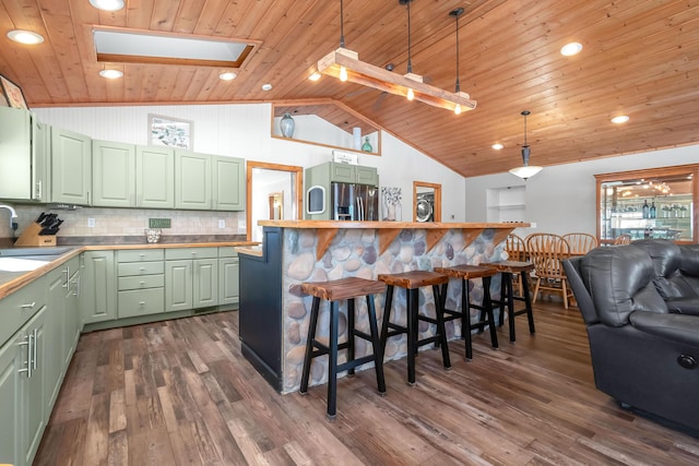 kitchen with decorative light fixtures, green cabinets, tasteful backsplash, a breakfast bar area, and stainless steel fridge