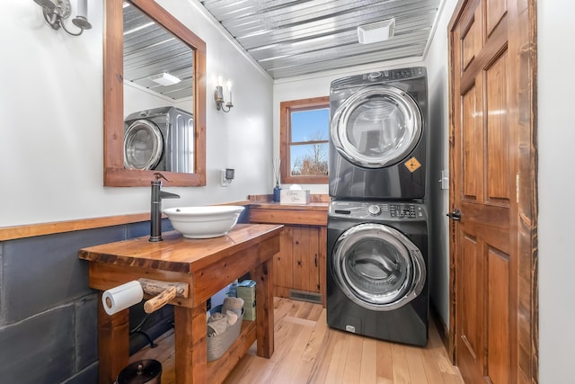 laundry area with light hardwood / wood-style flooring, stacked washer / dryer, and sink