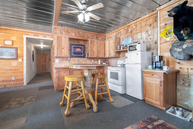 kitchen with white appliances, ceiling fan, wood walls, and dark colored carpet