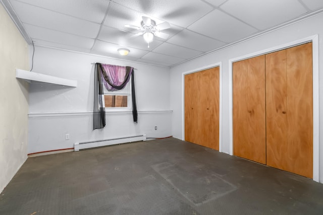 unfurnished bedroom featuring ceiling fan, a drop ceiling, multiple closets, and a baseboard heating unit