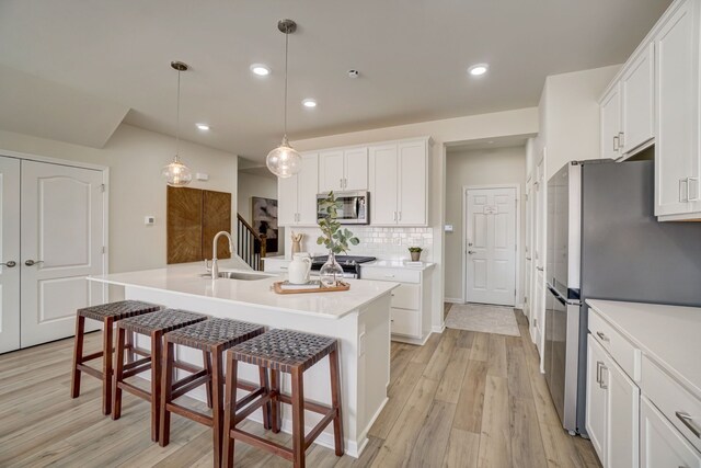 kitchen featuring stainless steel appliances, sink, white cabinetry, pendant lighting, and a kitchen island with sink