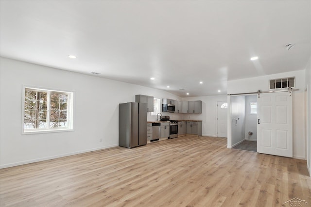 unfurnished living room featuring sink, a barn door, and light hardwood / wood-style flooring