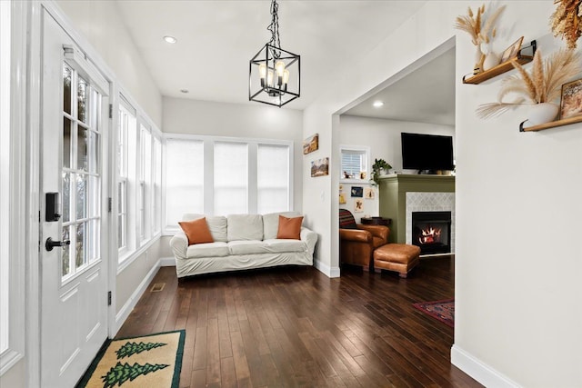 interior space featuring a tile fireplace, dark wood-type flooring, a chandelier, and a healthy amount of sunlight