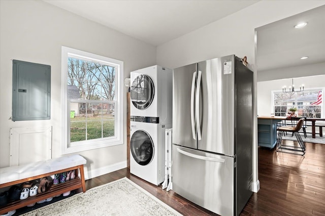 clothes washing area with electric panel, a healthy amount of sunlight, an inviting chandelier, and stacked washer and clothes dryer