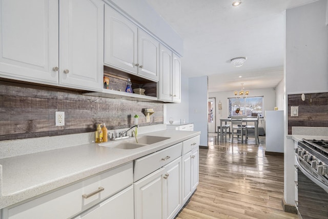 kitchen featuring tasteful backsplash, a notable chandelier, white cabinets, gas range, and sink