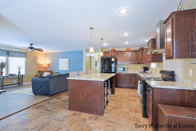 kitchen featuring a kitchen breakfast bar, black appliances, hanging light fixtures, a center island, and wall chimney range hood