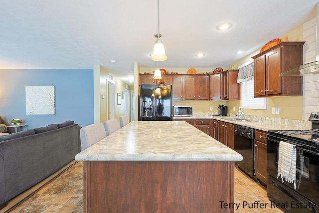 kitchen with black appliances, a kitchen island, sink, wall chimney range hood, and decorative light fixtures