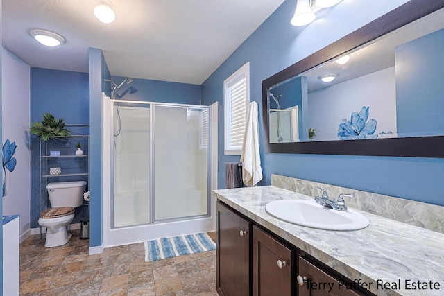 bathroom featuring a shower with door, vanity, and toilet