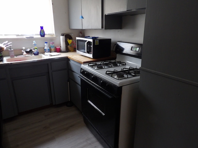 kitchen with gas stove, black fridge, gray cabinetry, and light hardwood / wood-style flooring