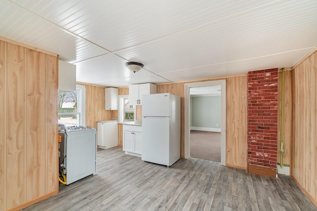 kitchen featuring white appliances, washer / clothes dryer, wood walls, light wood-type flooring, and white cabinetry