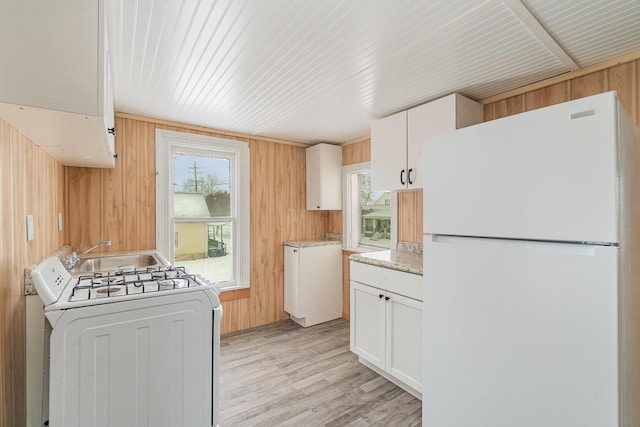 kitchen with white refrigerator, wood walls, white cabinetry, washer / clothes dryer, and sink