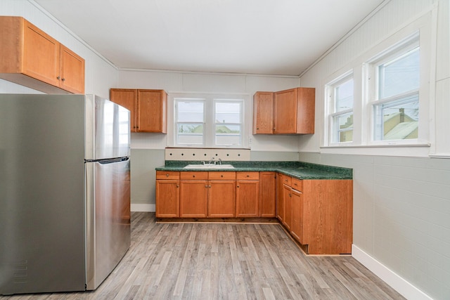 kitchen featuring sink, light wood-type flooring, ornamental molding, and stainless steel fridge