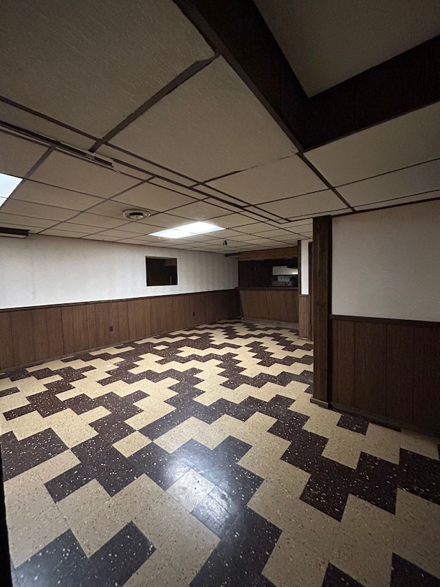 basement with a paneled ceiling and wood walls