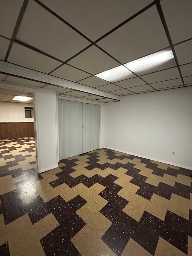 basement featuring a drop ceiling and wooden walls