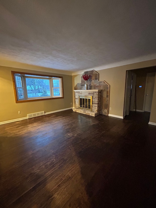 unfurnished living room featuring dark hardwood / wood-style flooring and a stone fireplace