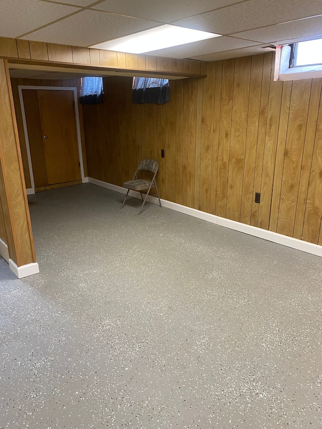 basement featuring a paneled ceiling and wood walls