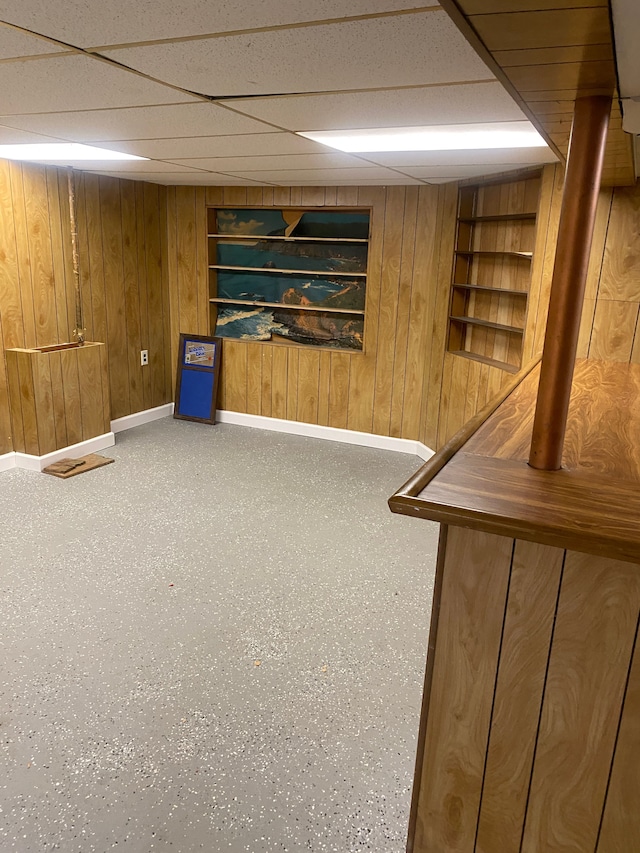 basement featuring a paneled ceiling, built in features, and wood walls